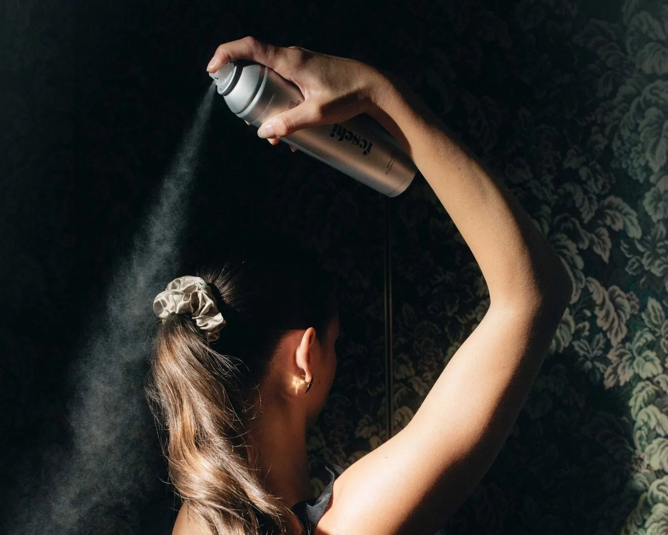 Person steht vor Tapete und sprüht sich die Haare mit dem feschi Haarspray en
