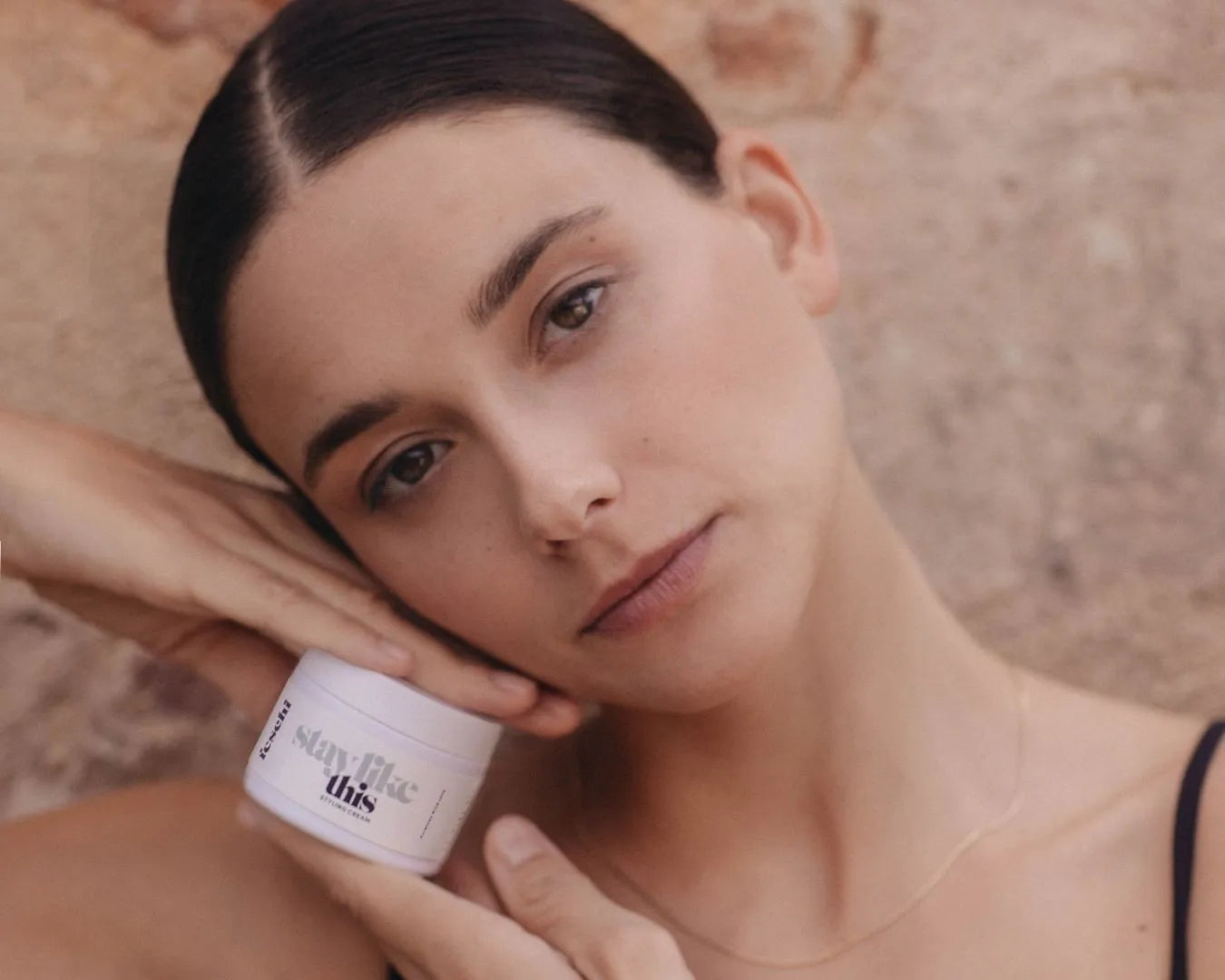 Frau vor rötlicher Steinwand, die die feschi Styling Cream in der Hand hält