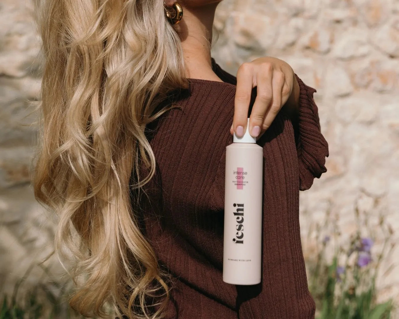 Frau von der Seite zu sehen mit blonden, langen und welligen Haaren mit dem intense care – Shampoo von feschi in der Hand