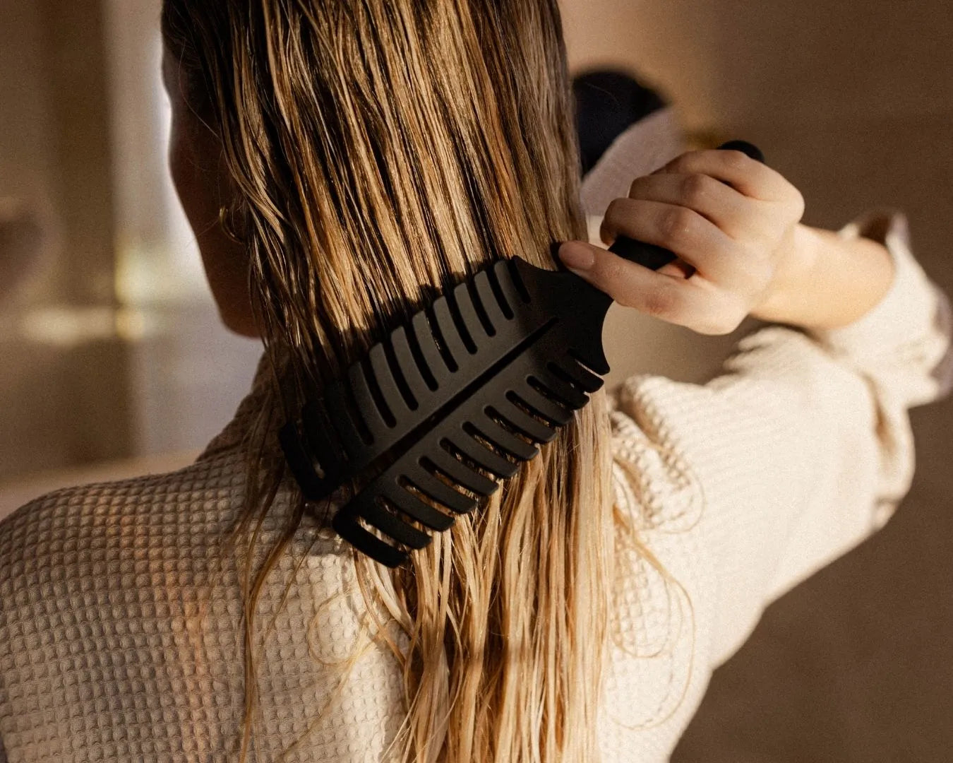 Frau bürstet ihre langen, nassen, dunkelblonden Haare mit der feschi Hair Brush, von hinten gesehen.