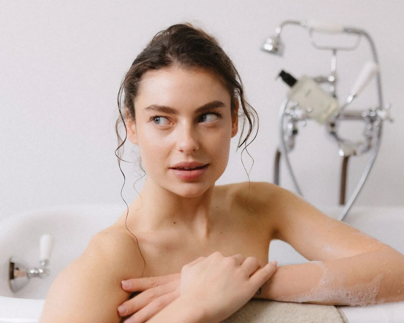 Frau sitzt in der Badewanne, lehnt am Rand und blickt zur Seite