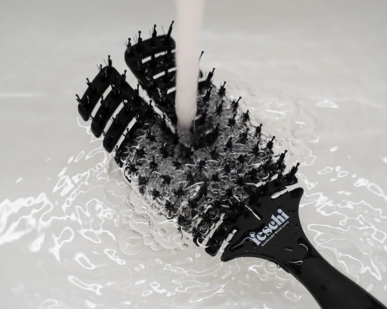 Produktbild der feschi The Essential Hair Brush unter einem Wasserhahn, Wasser läuft darüber