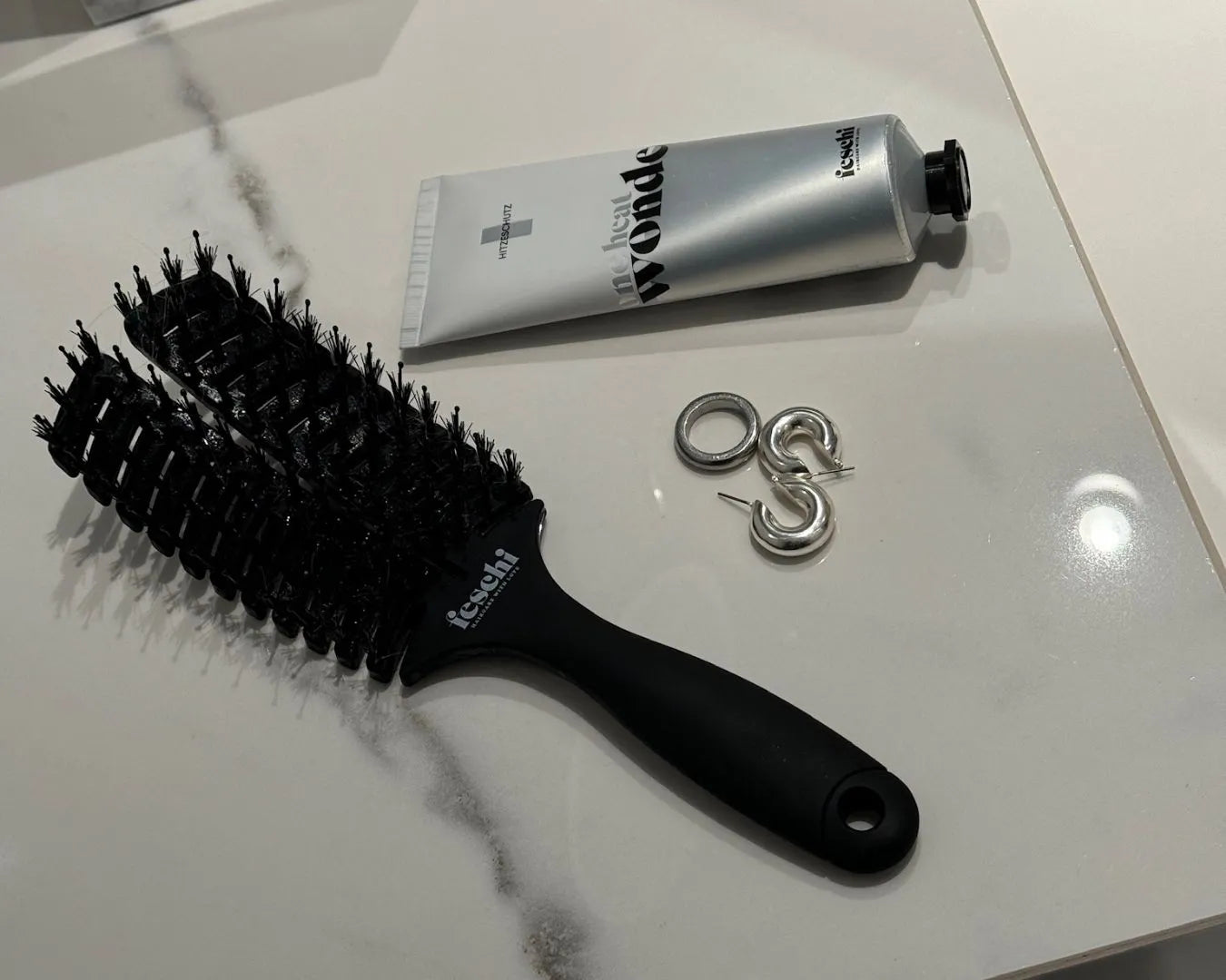 Produktbild der feschi The Essential Hair Brush und des One Heat Wonder Hitzeschutzes, liegend auf einer Fliese