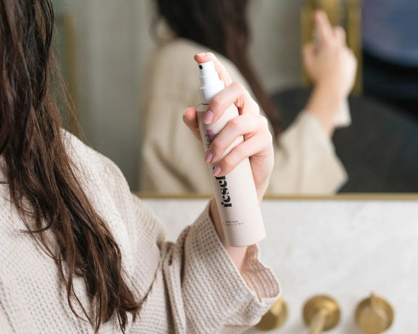 Ein Pflegespray von feschi wird im Badezimmer in den handtucktrockenen Haaren angewendet
