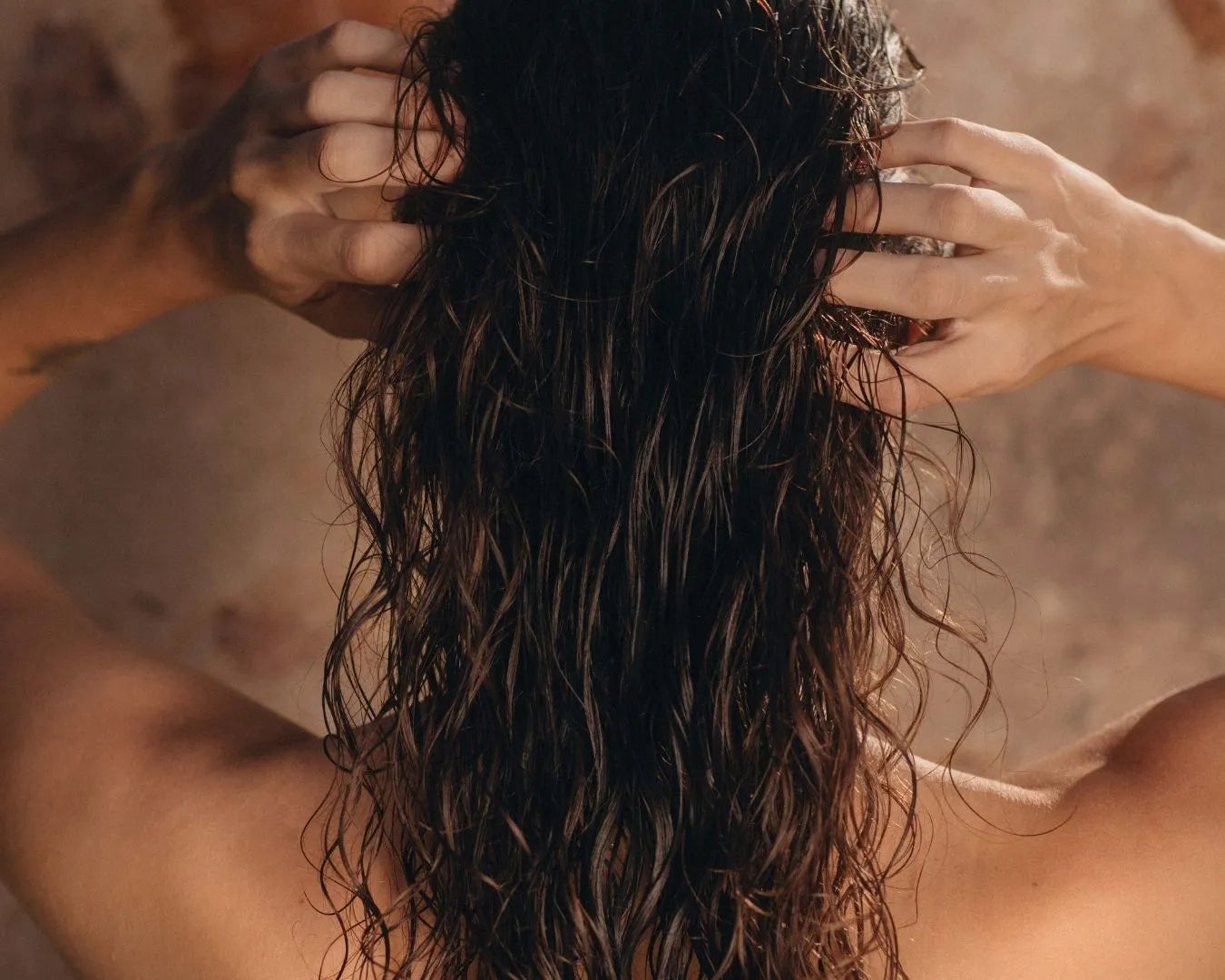 Person mit lockigen, nassen Haaren von hinten vor Steinwand stehend