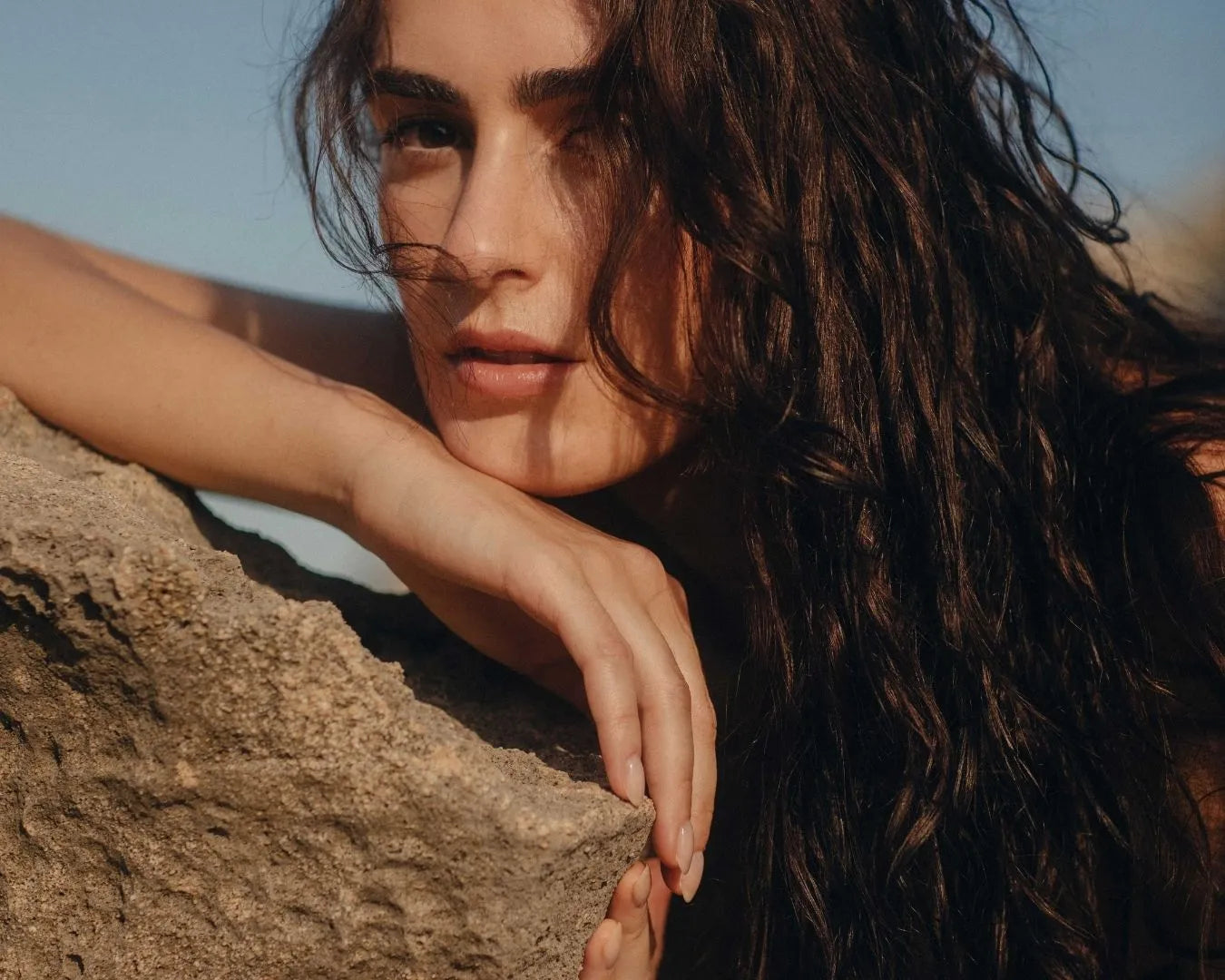 Frau mit dunklen Locken lehnt auf Stein