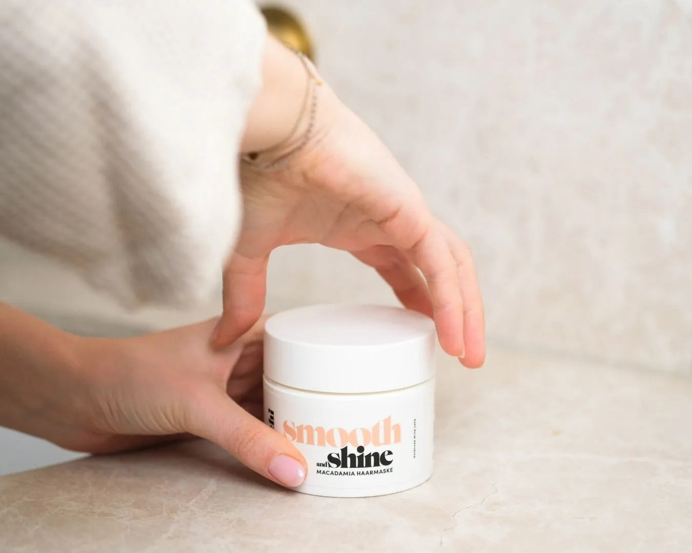 Weibliche Hand hält die feschi Smooth & Shine Maske, die andere Hand dreht den Verschluss auf.