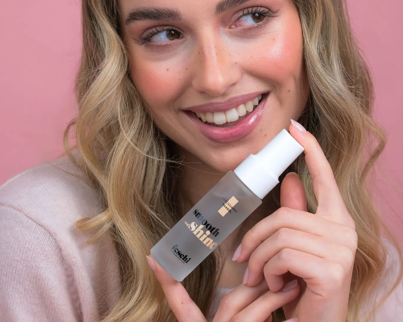 Person hält smooth & shine - Macadamia Haaröl von feschi in der Hand und lächelt in Kamera