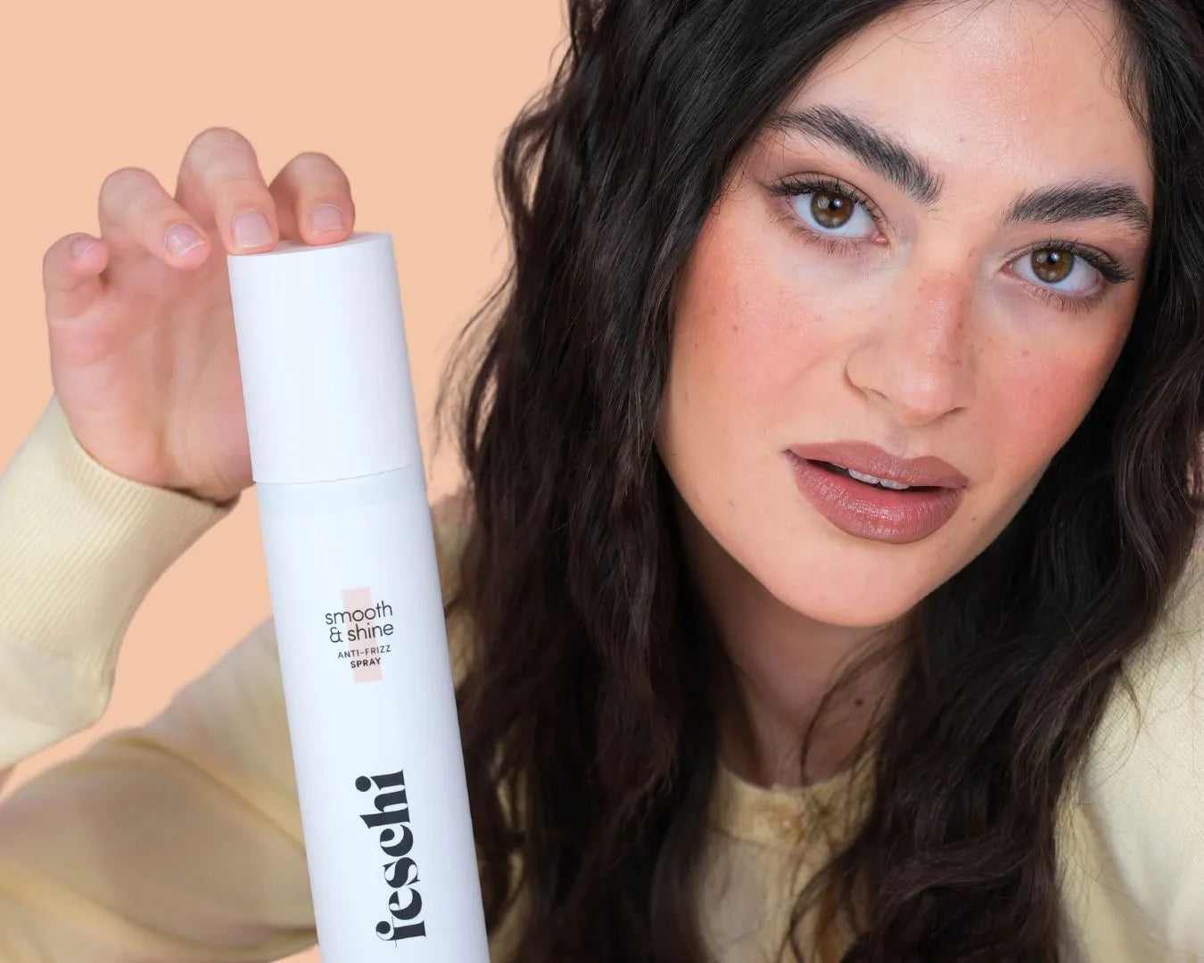 Frau mit dunklen, glänzenden Haaren hält Anti Frizz Spray in der Hand