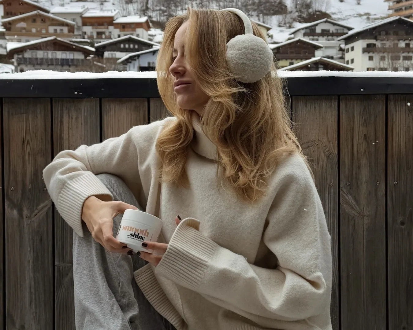 Frau mit blonden Haaren sitzt vor Winterlandschaft und hält eine feschi Haarmaske in der Hand