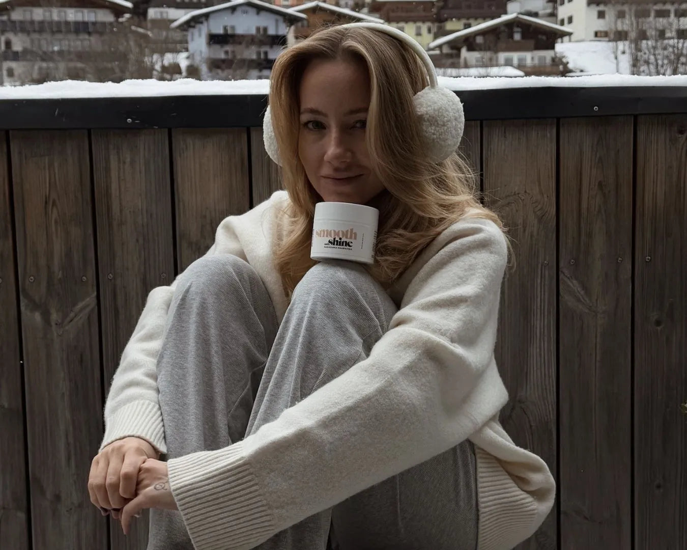 Frau sitzt auf Balkon vor Winterlandschaft und stützt sich mit dem Kinn an einer Haarmaske von feschi ab