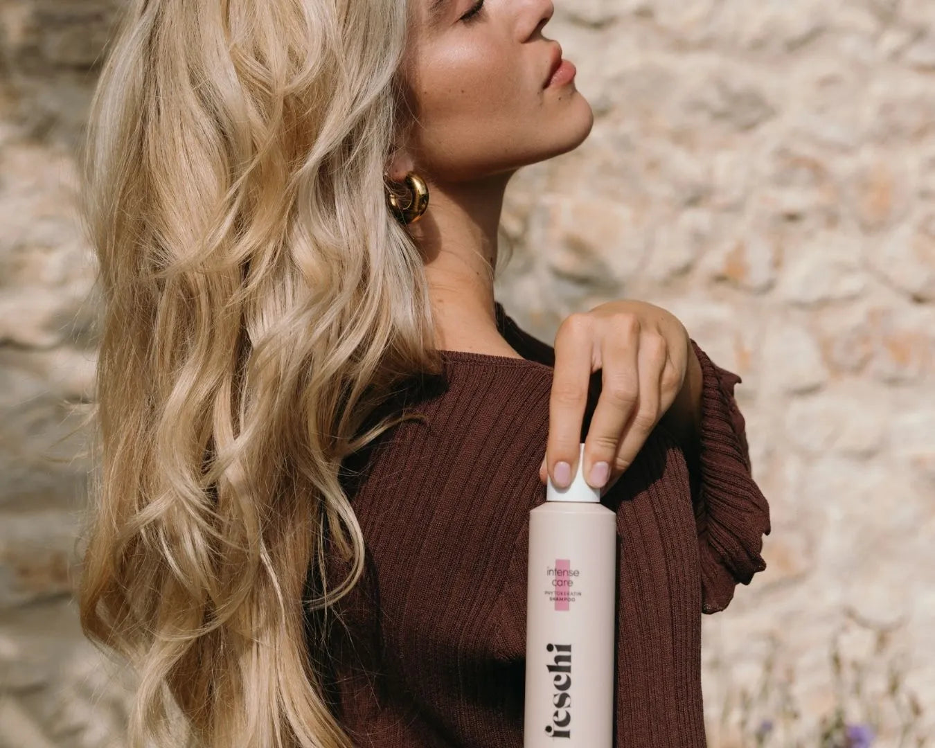Frau mit blonden langen Haaren und braunem Kleid hält Produkt von feschi in der Hand und lässt es über Schultern fallen