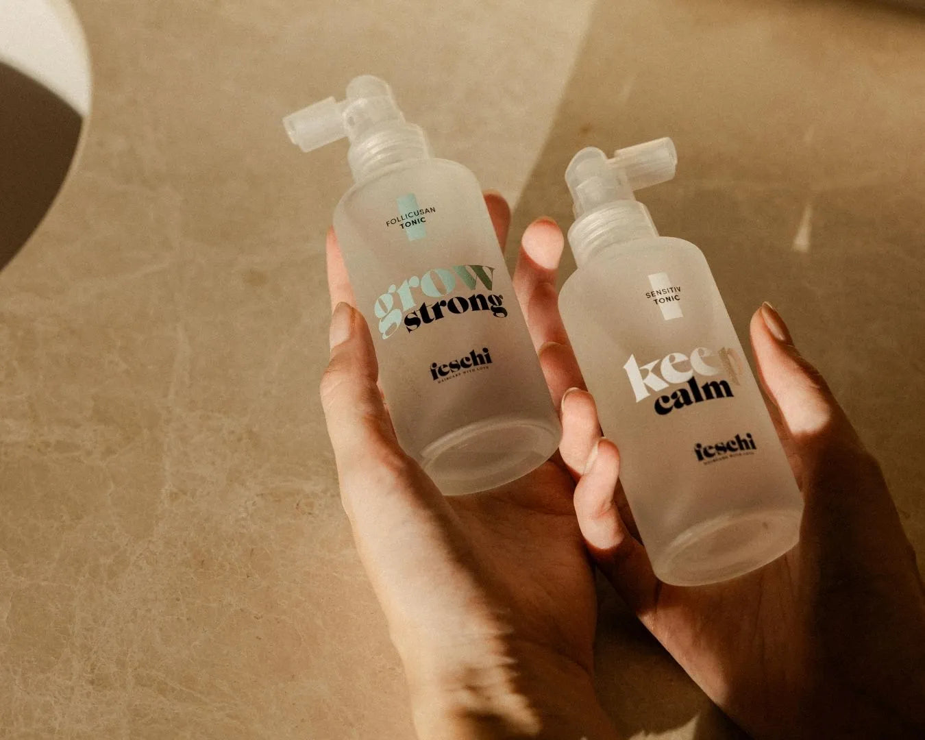 Zwei Hände halten jeweils das feschi Grow Strong Follicusan Tonic und das Keep Calm Sensitiv Tonic