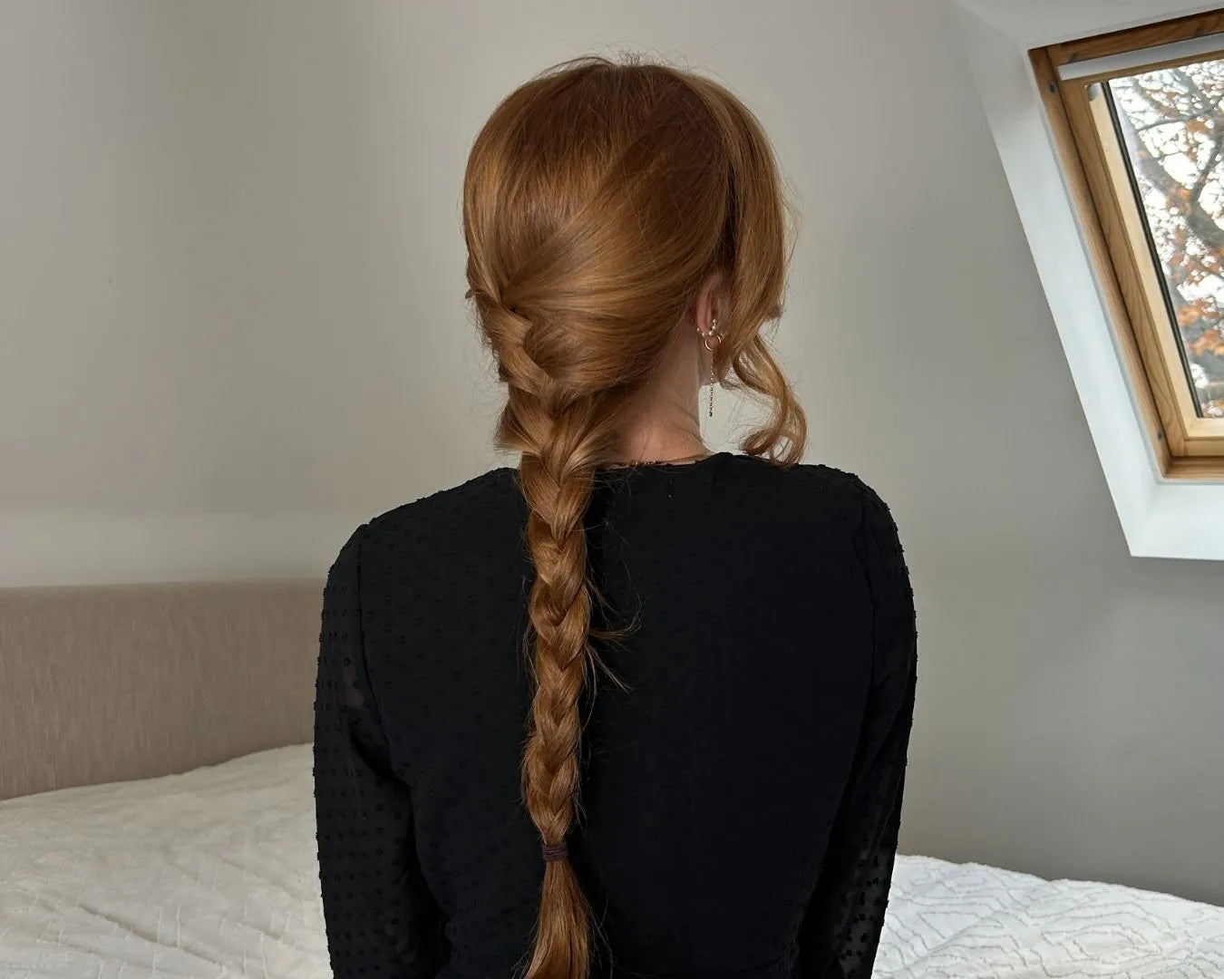 Frau von hinten, sitzend auf dem Bett, mit langen roten Haaren zu einem geflochtenen Zopf