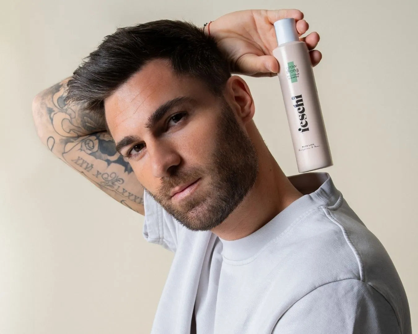 Mann mit Tattoos am Arm, der eine feschi Shampoo Flasche hinter seinem Kopf hält