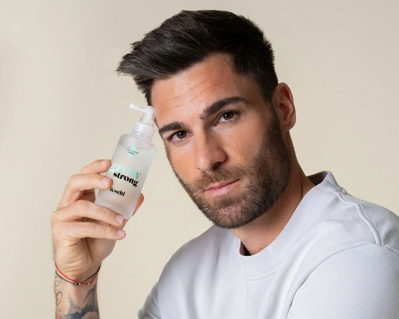 Man mit gestylten, kurzen Haaren, hält das grow strong - Follicusan Tonic in der Hand und stützt sich dabei mit dem Kopf ab