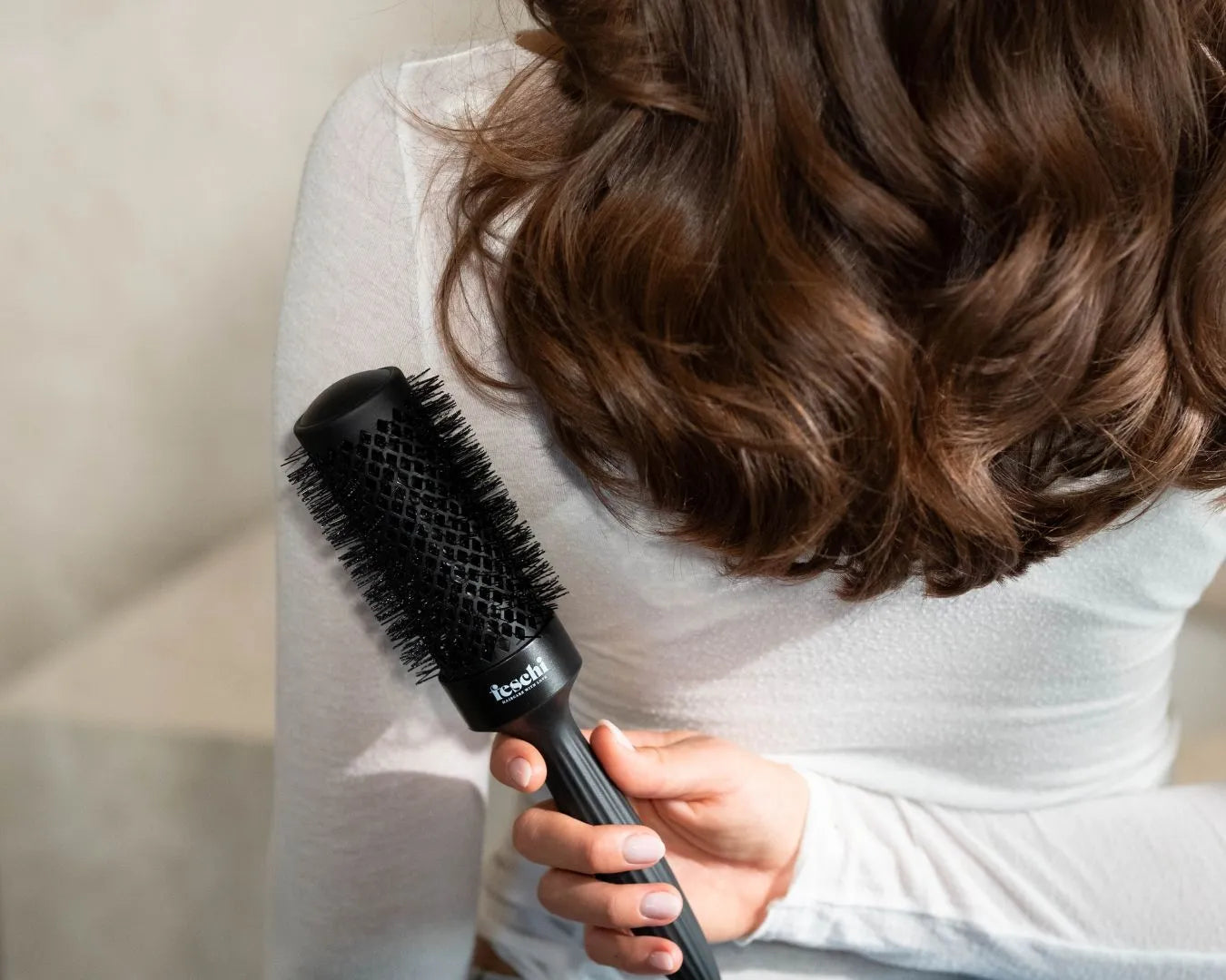 Person mit längeren, brünetten Haaren hält die Rundbürste hinter ihrem Rücken