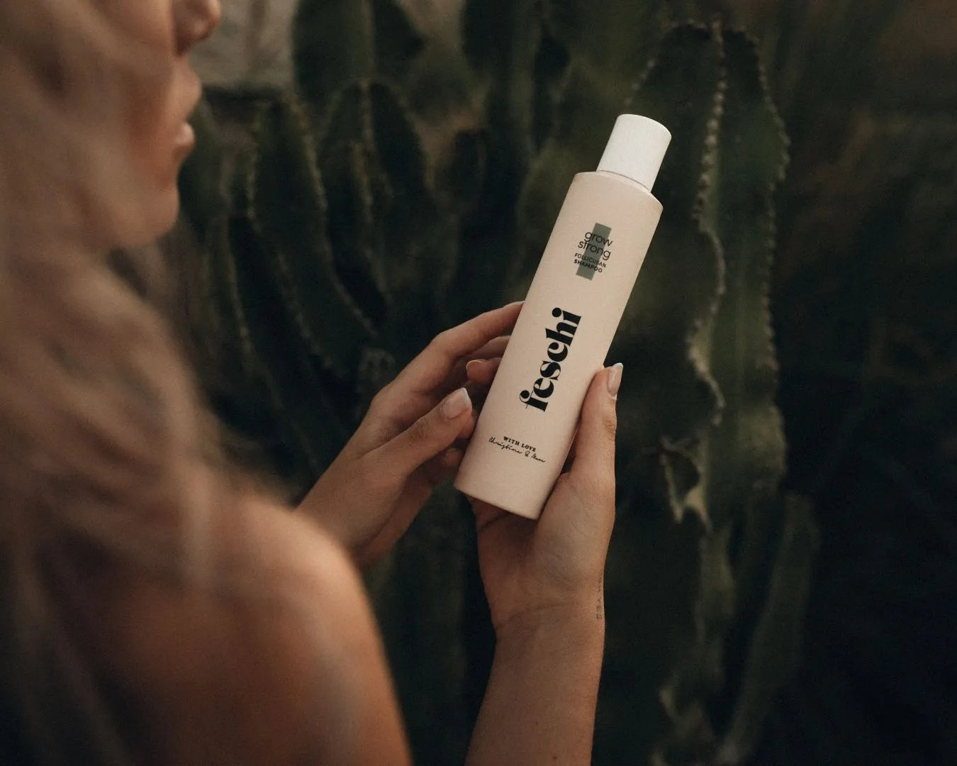 Frau, halb von hinten zu sehen, hält das feschi Grow Strong Follicusan Shampoo in beiden Händen