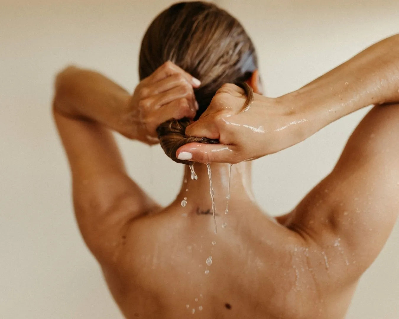 Frau beim Haarewaschen in der Dusche von hinten zu sehen