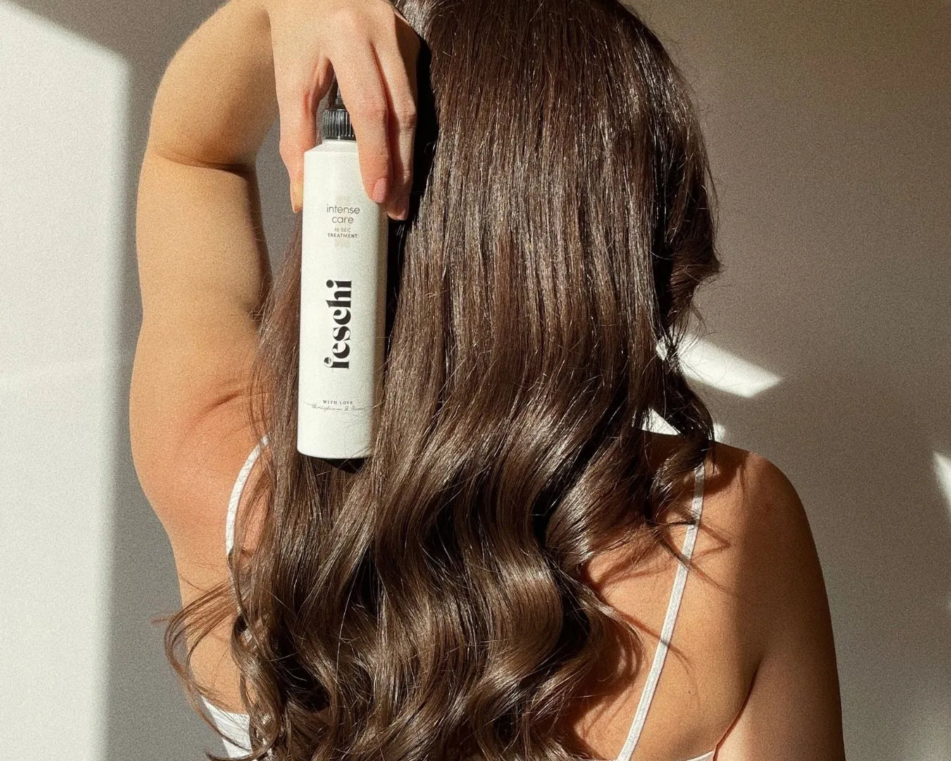 Frau von hinten zu sehen mit dunkelbraunen, langen und welligen Haaren mit der 10 Second Treatment von feschi in der Hand