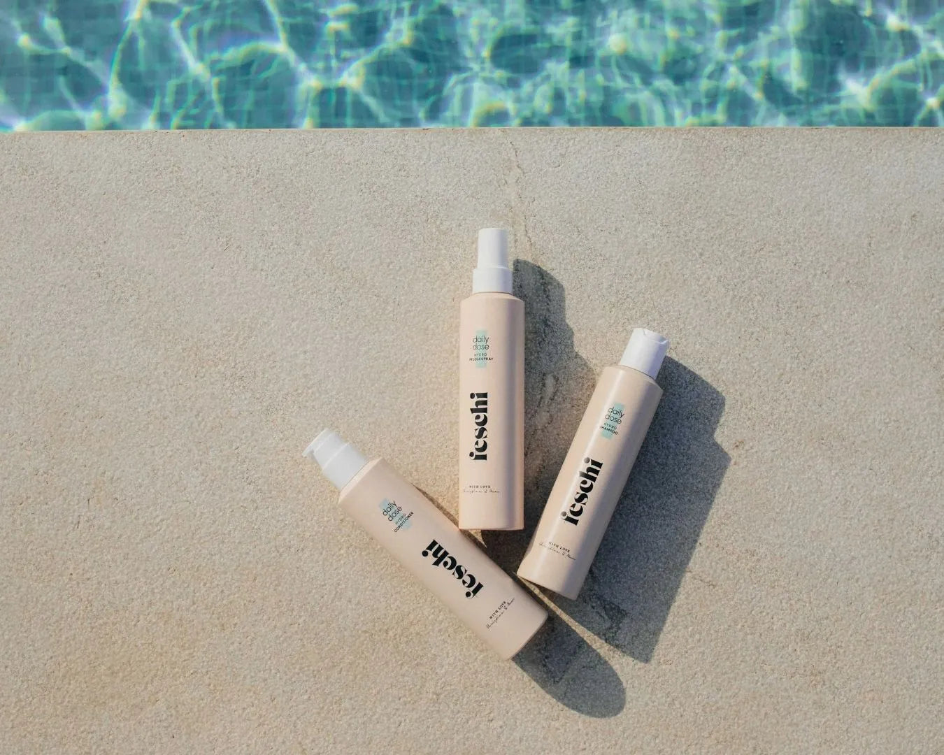 Produktbild der feschi Daily-Dose Serie mit Shampoo, Conditioner und Pflegespray am Poolrand, Wasser im Hintergrund