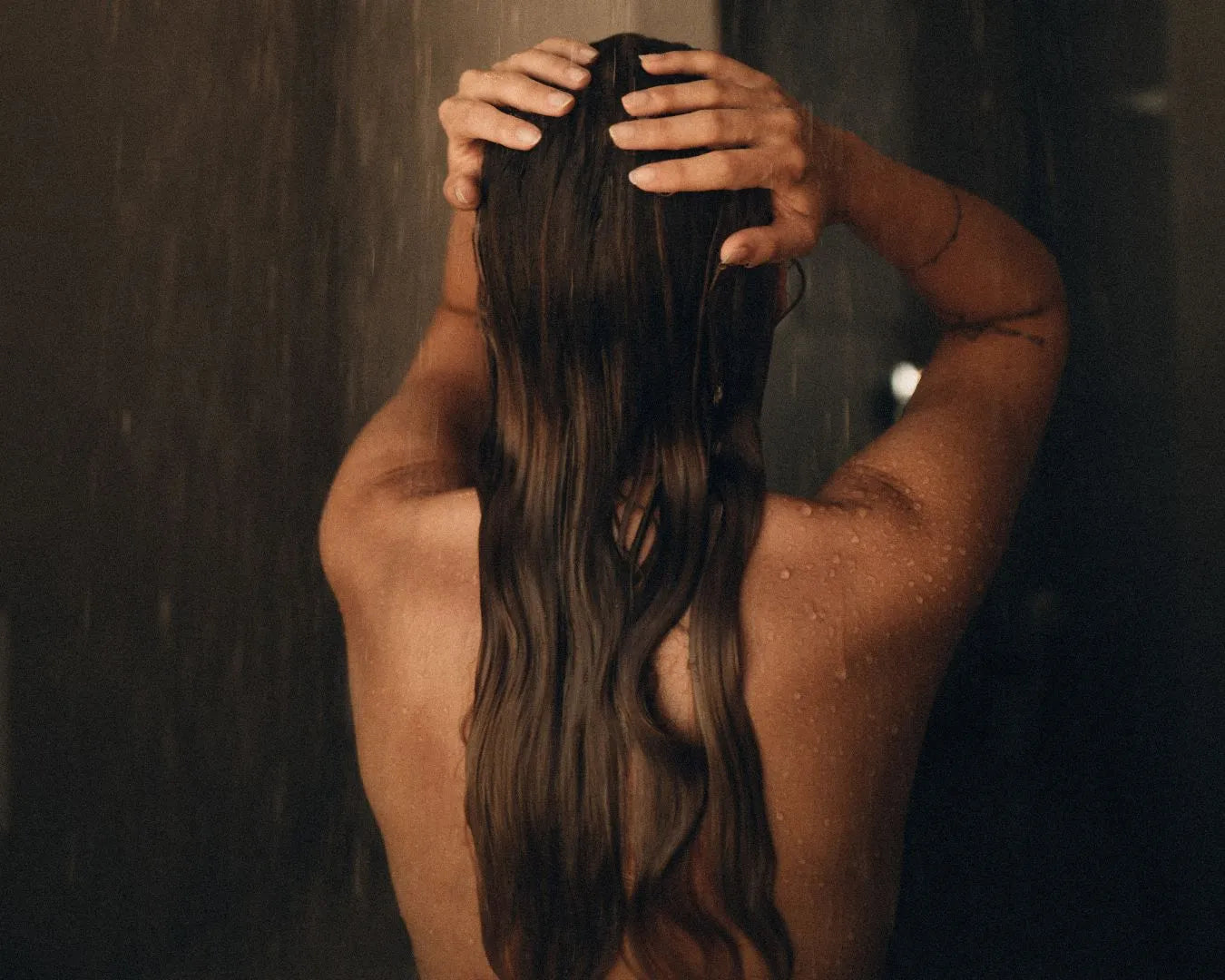 Frau von hinten steht in der Dusche und wäscht ihre Haare