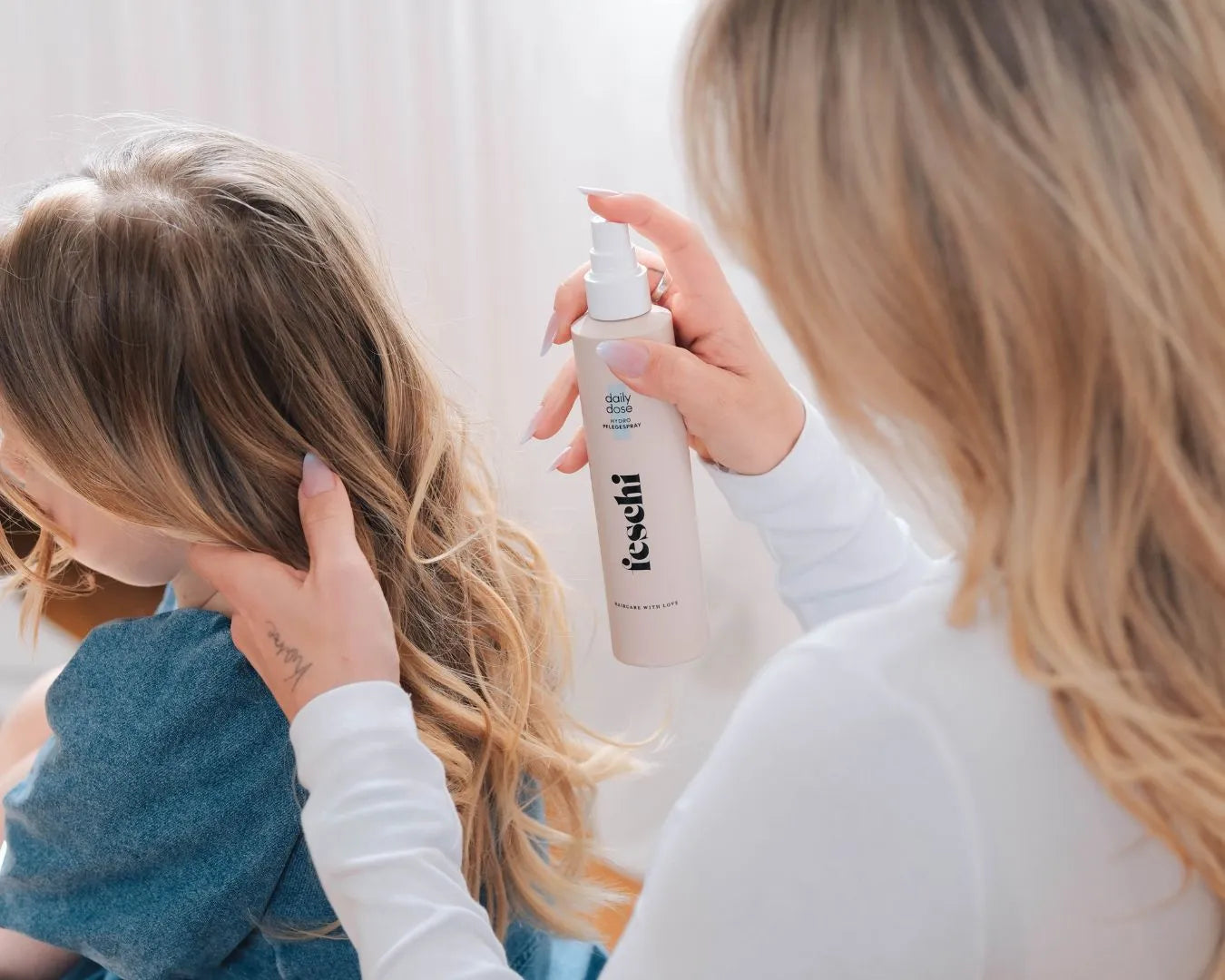 Frau sprüht daily dose Pflegespray von feschi in Haare von Kind