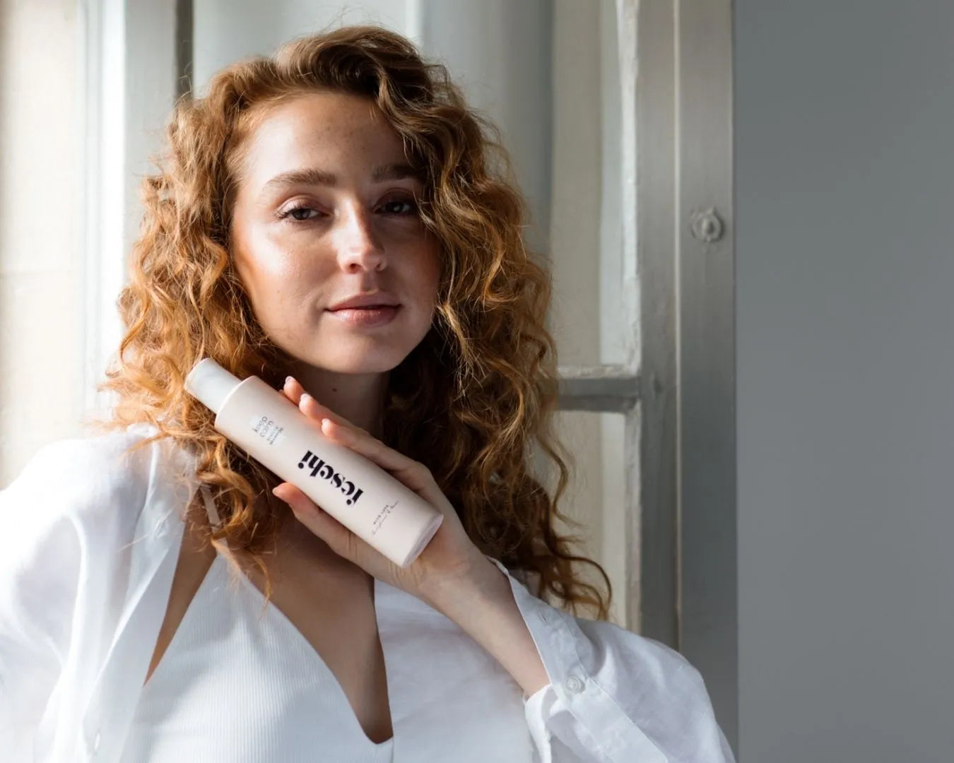 Frau hält das feschi keep calm - Sensitiv Shampoo in der Hand und trägt dabei eine weiße Leinenbluse mit einem weißen Bralette