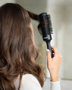 Person mit braunen Haaren wickelt Haarsträhne um Rundbürste