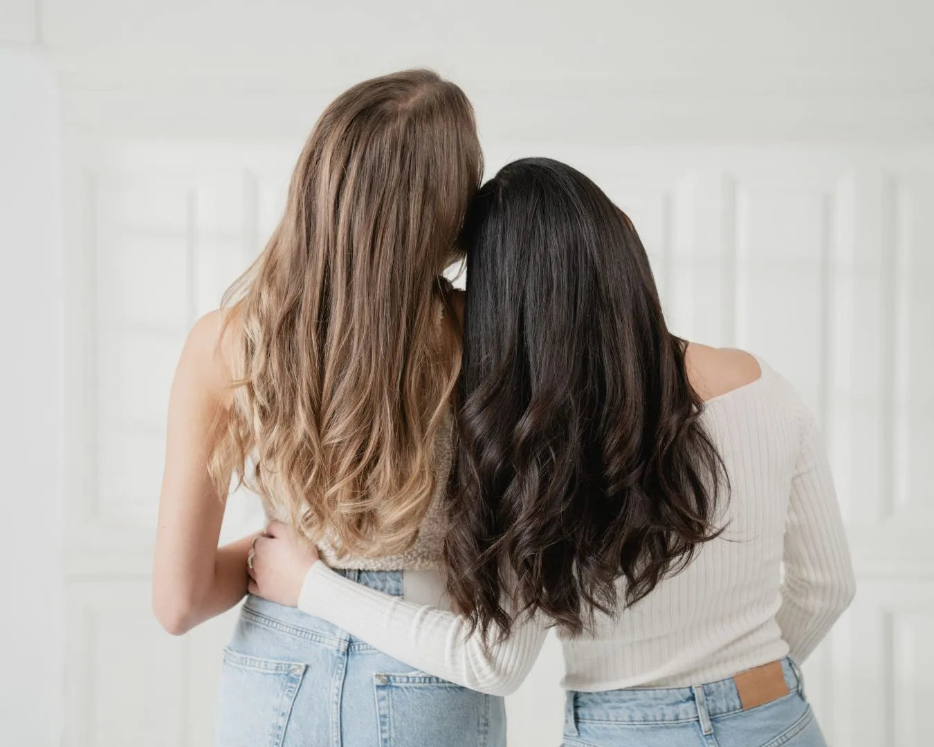 blonde und dunkelhaarige Frauen sind von hinten zu sehen und halten sich in den armen