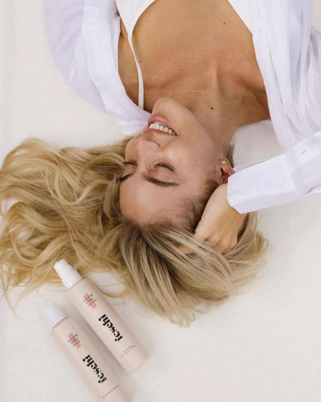 Blonde Frau mit langen Haaren und feschi Haircare Produkten auf weißem Hintergrund