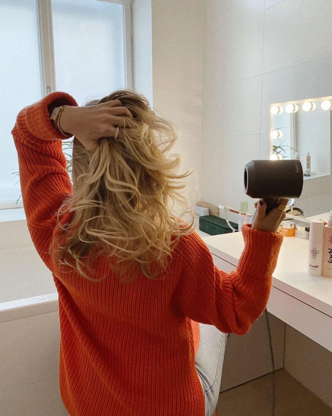 Frau von hinten föhnt ihre blonden Haare im Badezimmer