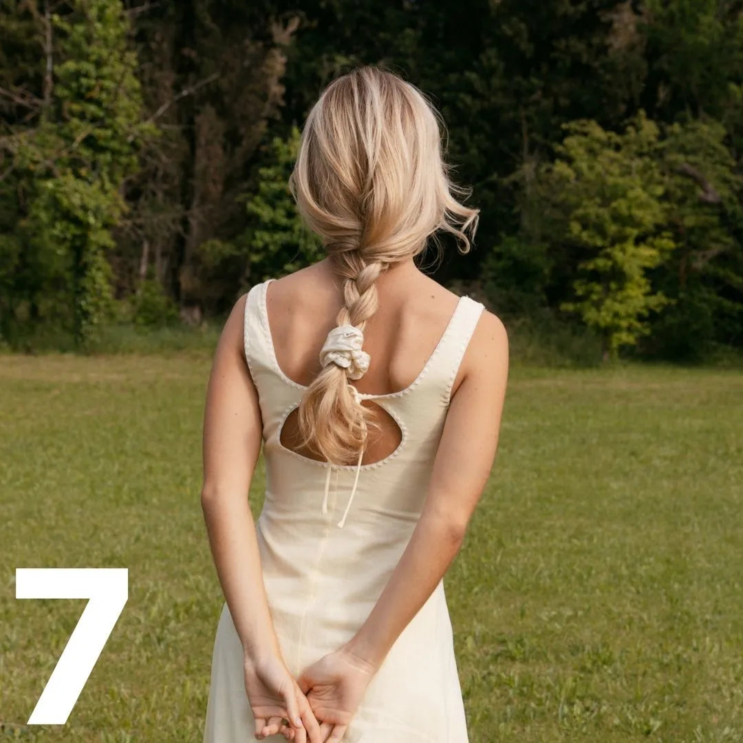 Frau von hinten mit verschränkten Armen im Rücken, trägt einen geflochtenen Zopf mit weißem Seiden-Scrunchie von feschi