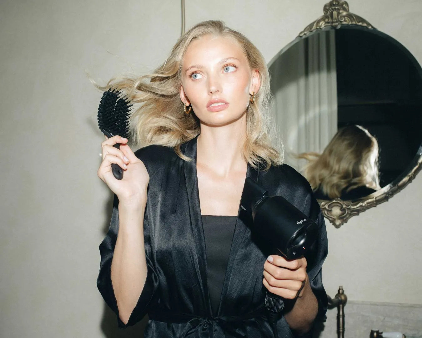 Frau mit langen blonden Haaren hält in der einen Hand einen Föhn und in der anderen die feschi The Essential Hair Brush

