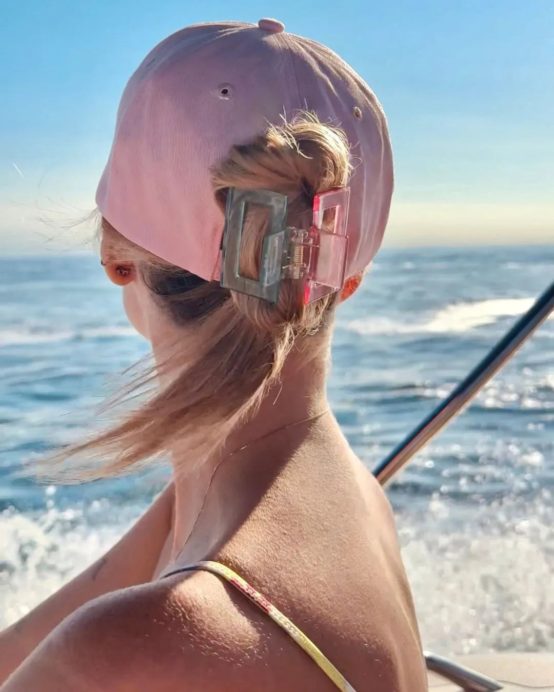 Frau von hinten, sitzend auf einem Boot, trägt eine rosa Kappe und die feschi Butterfly Spange