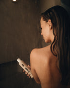 Frau steht in Dusche und hält grow strong Shampoo von feschi in der Hand