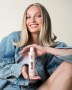 Frau mit glattem, blondem Haar präsentiert das feschi Phytokeratin Shampoo und lächelt in die Kamera