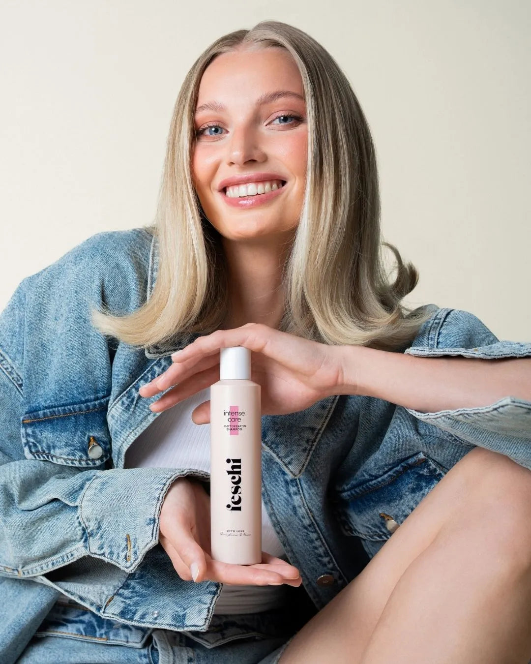 Frau mit glattem, blondem Haar präsentiert das feschi Phytokeratin Shampoo und lächelt in die Kamera