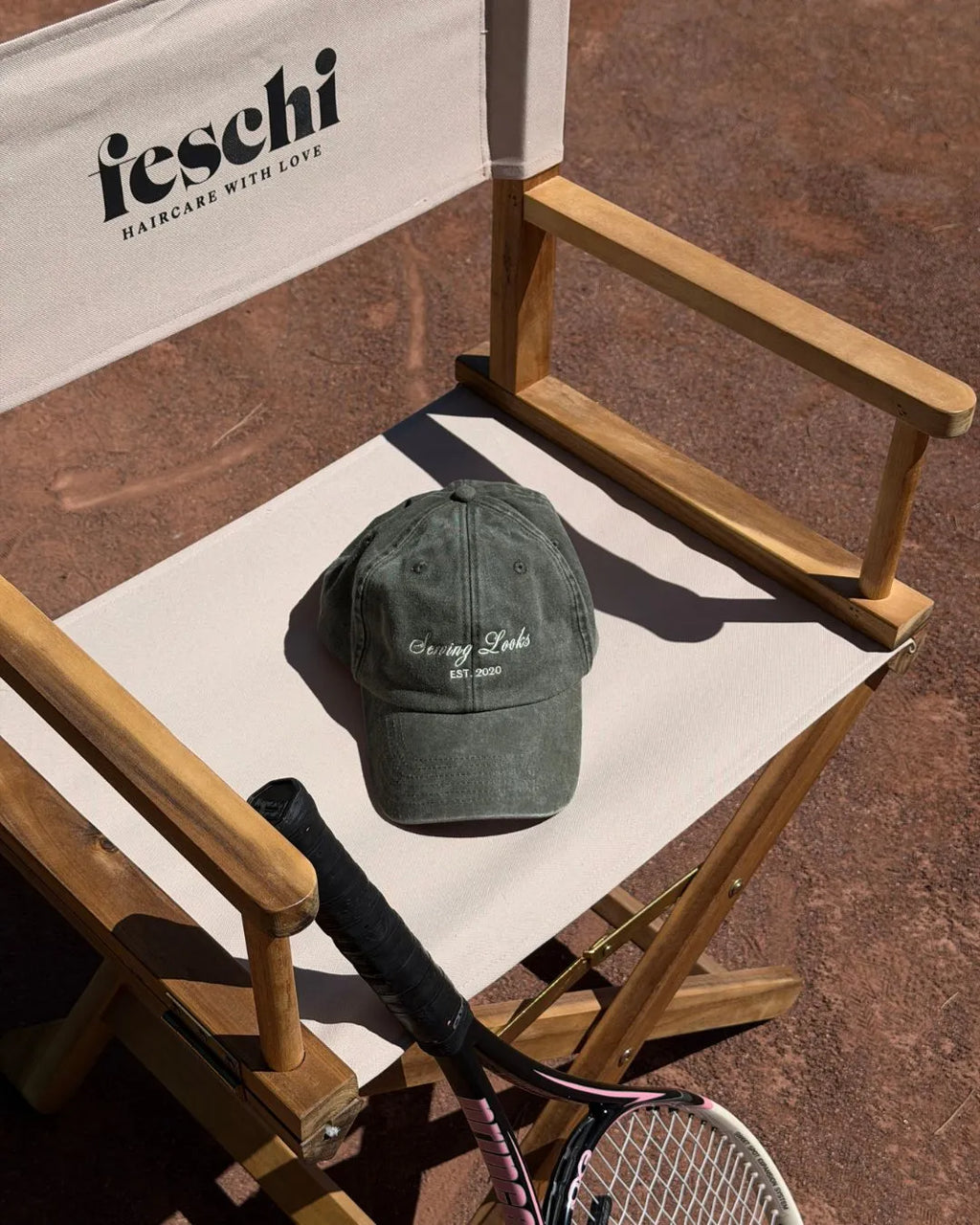 Stuhl mit feschi Logo steht auf rotem Sandboden und darauf liegt eine Vintage-Kappe in grün von feschi