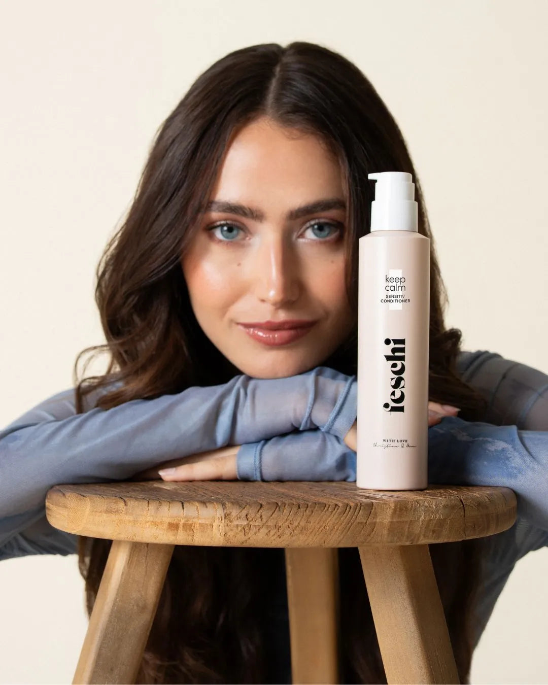 frau mit dunklen langen haaren, lehnt an holzstuhl und vor ihr steht der keep calm - sensitiv conditioner