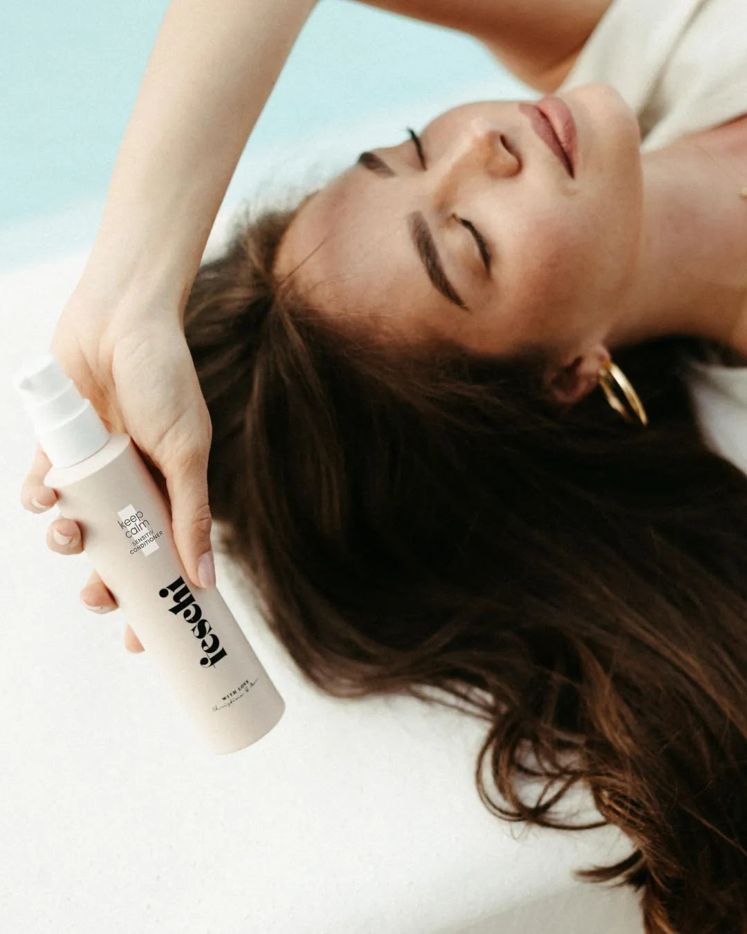 frau mit dunklen, langen haaren liegt am boden und hält den keep calm - sensitiv conditioner über ihren kopf