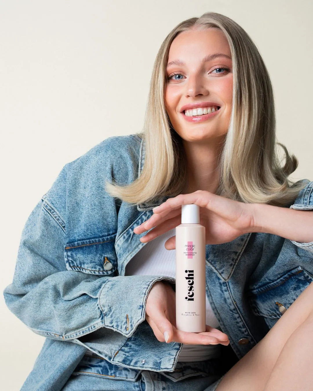 Frau mit schönen blonden Haaren lächelt in Kamera und hält das magic color Shampoo von feschi in der Hand