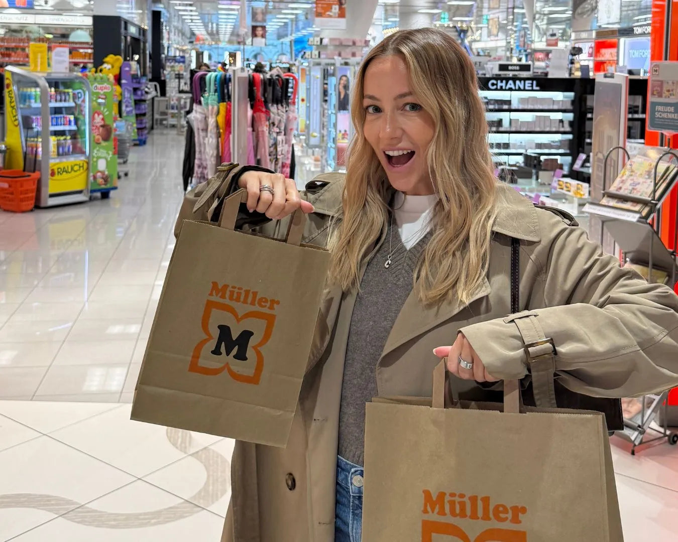 Christina Bischof steht vor Müller Filiale und präsentiert Müller Tüten gefüllt mit feschi Produkten