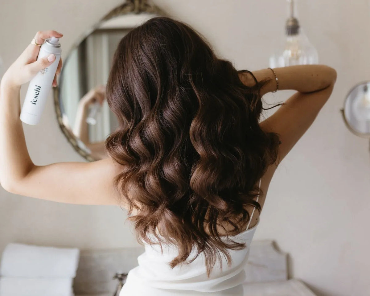 braunhaariges Model mit langen, glänzenden Locken sprüht den feschi Anti Frizz Spray in ihr Haar
