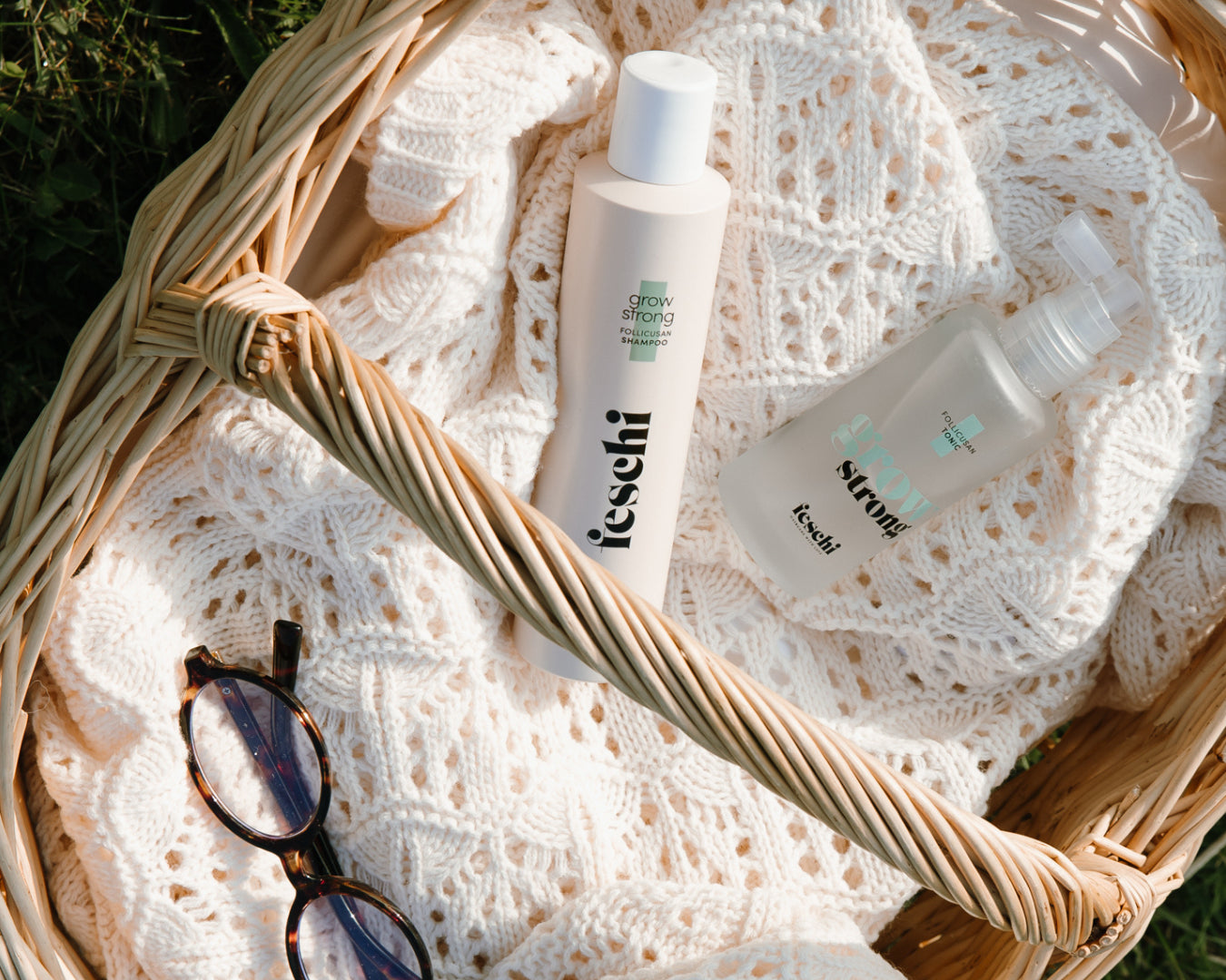 geflochtener Korb steht auf grüner Wiese, gefüllt mit feschi grow strong Shampoo und Tonic. 