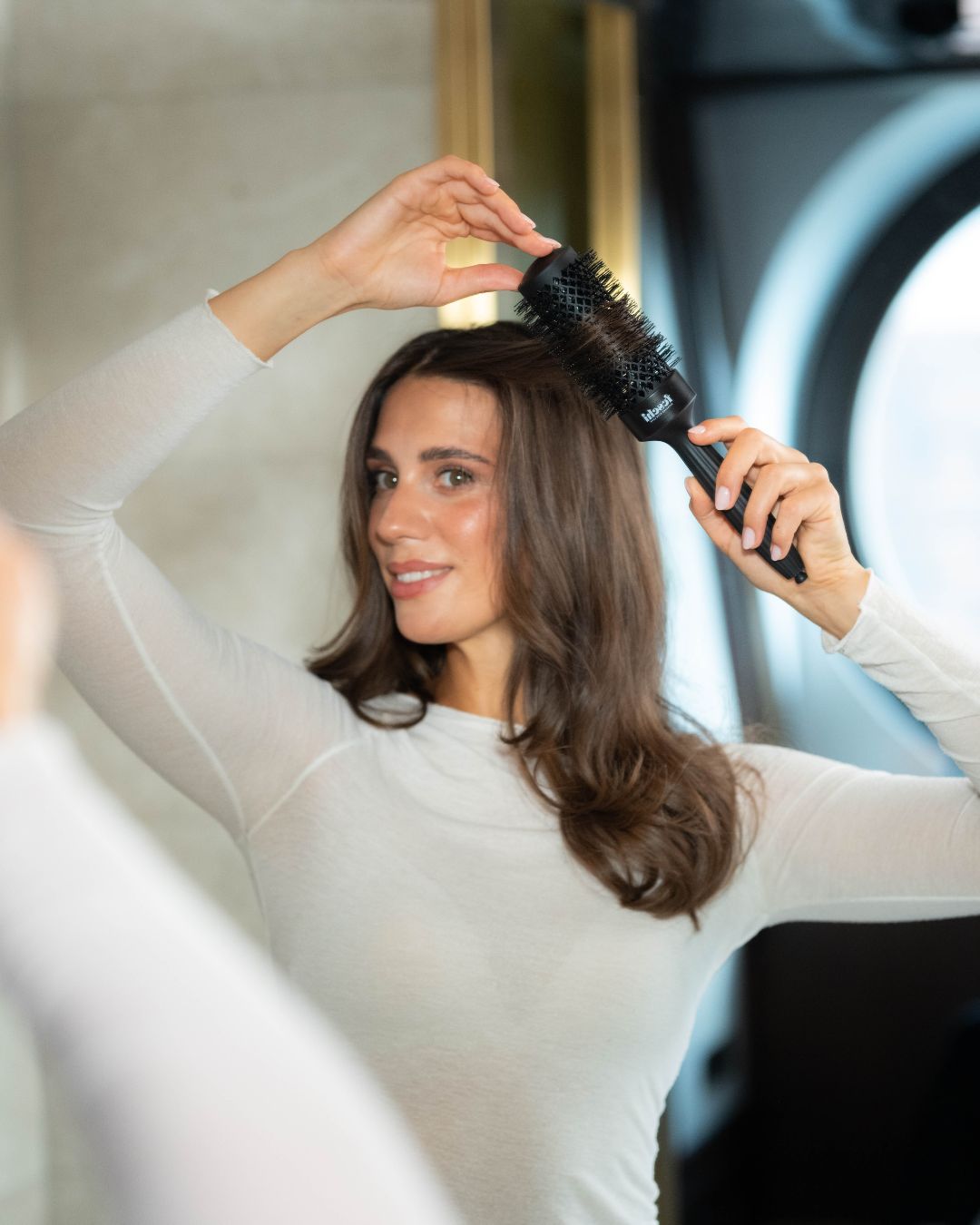 Frau hält feschi Rundbürste in Hand und dreht sich Haare ein