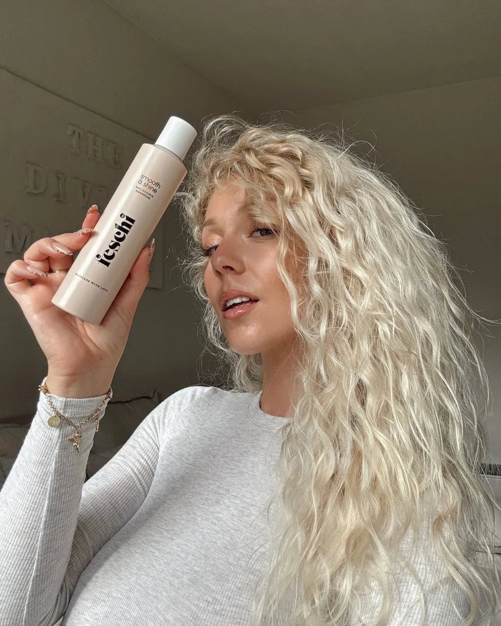 Frau mit langen, blonden, lockigen Haaren hält smooth & shine Macadamia Shampoo in den Händen