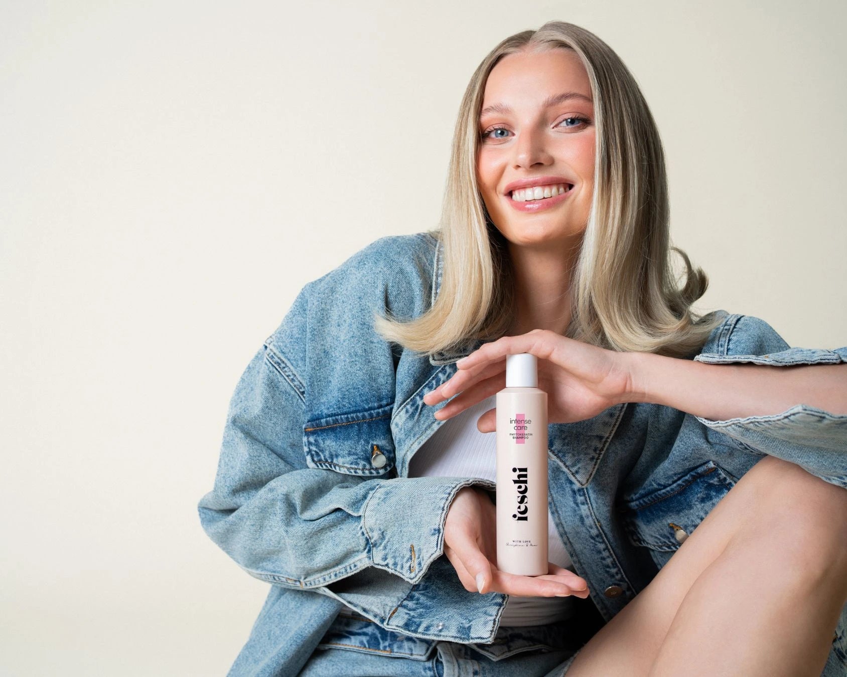 Frau mit blonden Haaren hält feschi Shampoo in der Hand und lächelt in Kamera