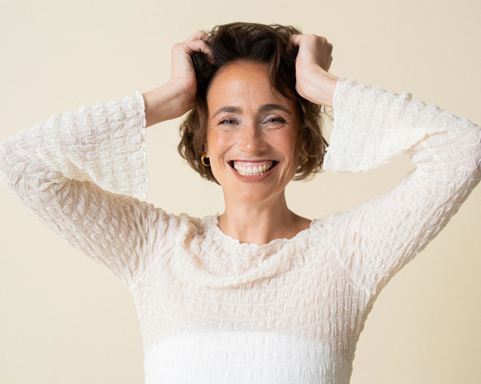 Frau mit kurzen Haaren fasst sich in Haare und grinst