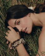 Frau liegt auf der Wiese, blickt in die Kamera und trägt an den Handgelenken die The Silk Edit Seidenscrunchies von feschi